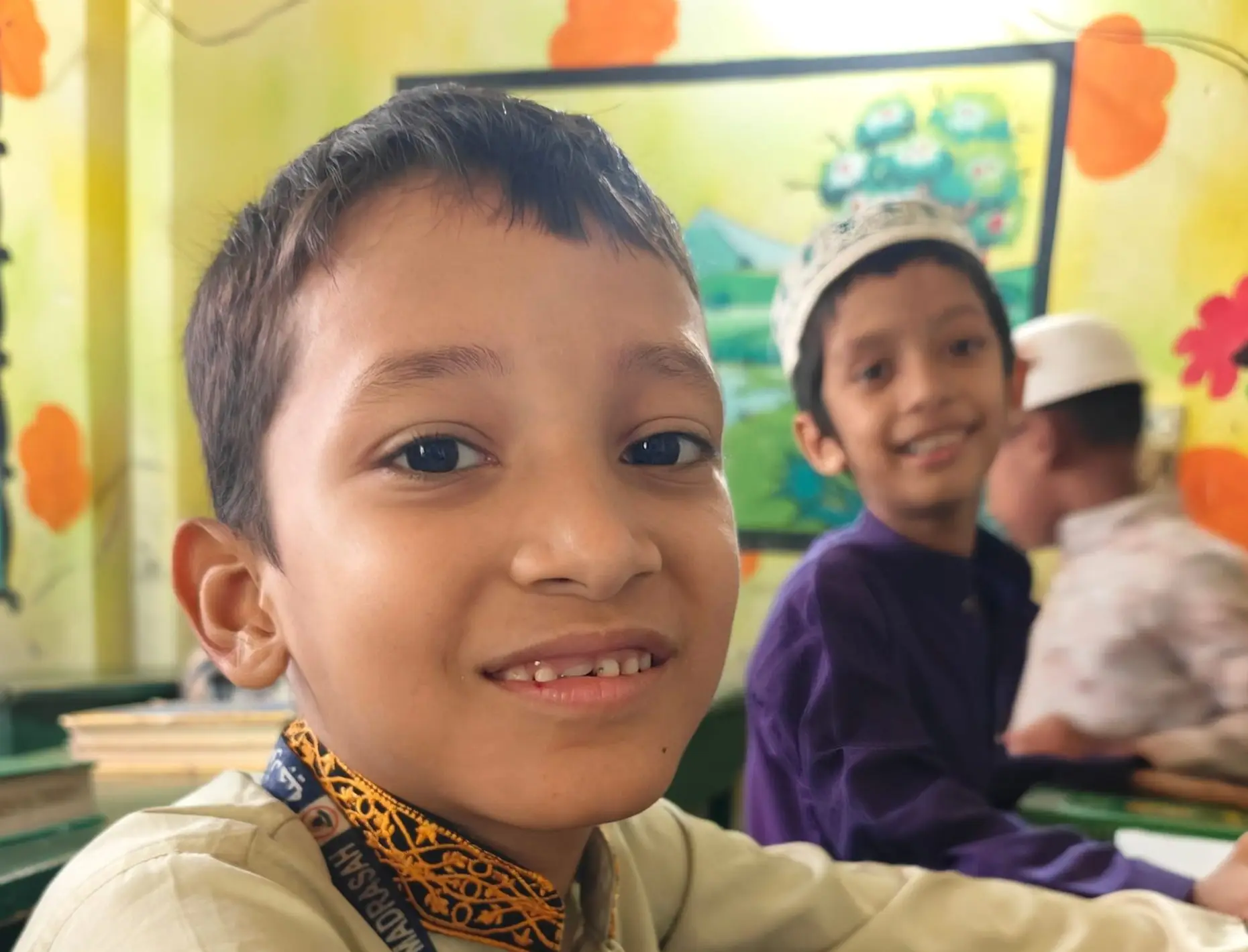 Two children smiling in a colorful classroom, wearing traditional attire.